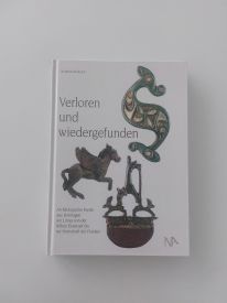 Das Buch zeigt Archäologische Funde aus Dormagen am Limes von der frühen Eisenzeit bis zur Herrschaft der Franken Ein geschlossenes Buch auf einem Tisch, mit einem einfachen Cover-Design. Der Titel "Verloren und wiedergefunden" ist deutlich sichtbar und das Buch scheint in gutem Zustand zu sein, bereit zum Lesen oder zur Aufbewahrung in einer Bibliothek.